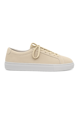 A low-top sneaker in light beige leather with matching beige laces and a thick white sole, shown from a side profile on a white background.